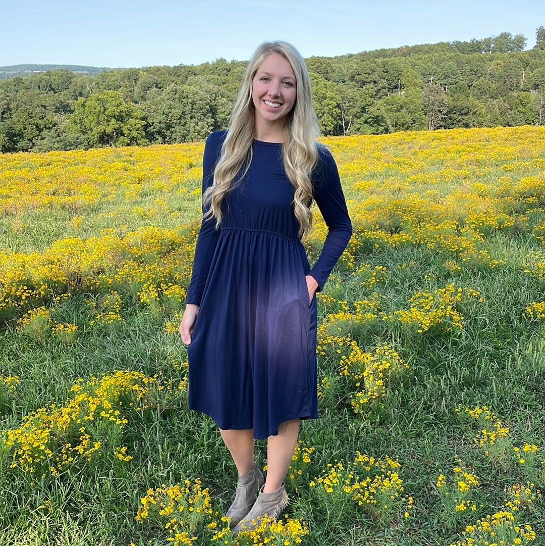 Long sleeve navy dress. Made with butter soft material. Elastic waist with pockets. Scoop hemline that falls below the knee. Perfect for pairing with and accent belt or scarves. This is a size up dress.